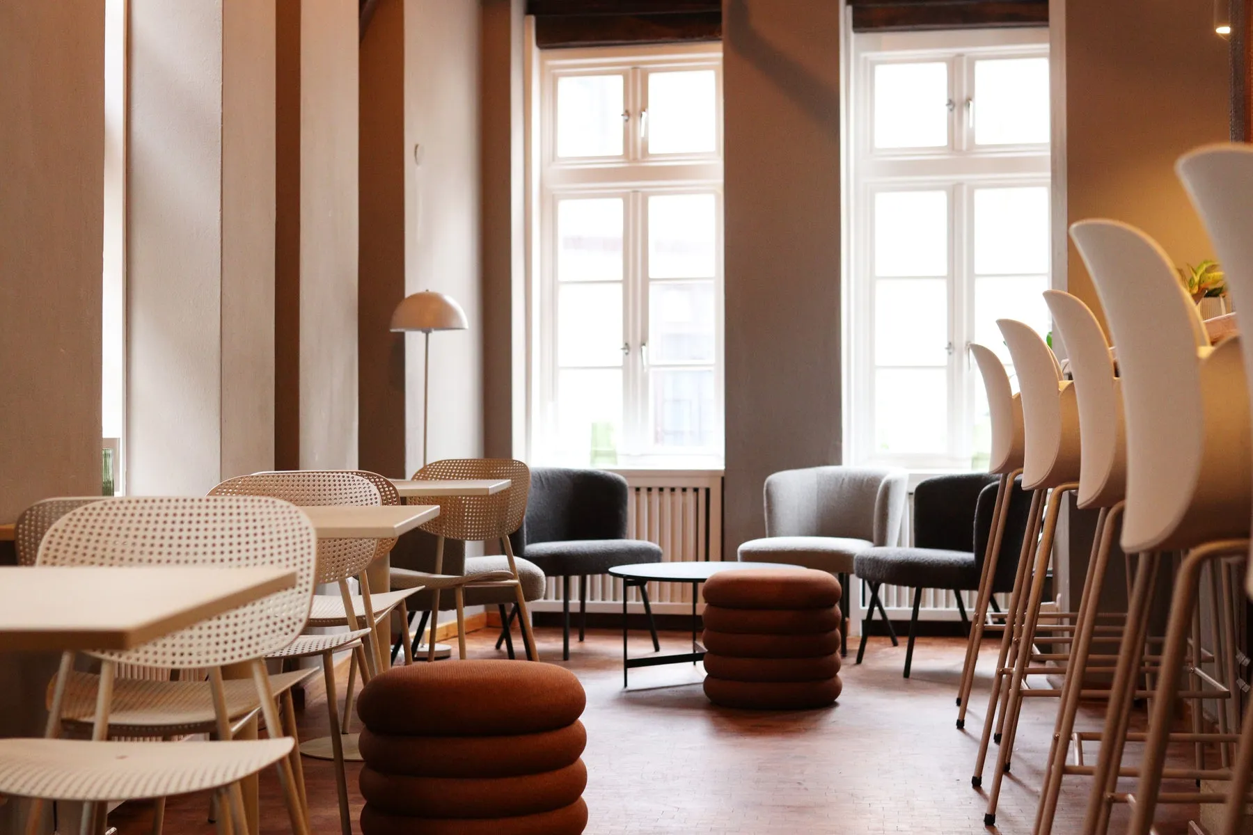 Gastraum des kofi Museumscafés mit hellen Stühlen, Terrakotta-Hockern und großen Sprossenfenstern