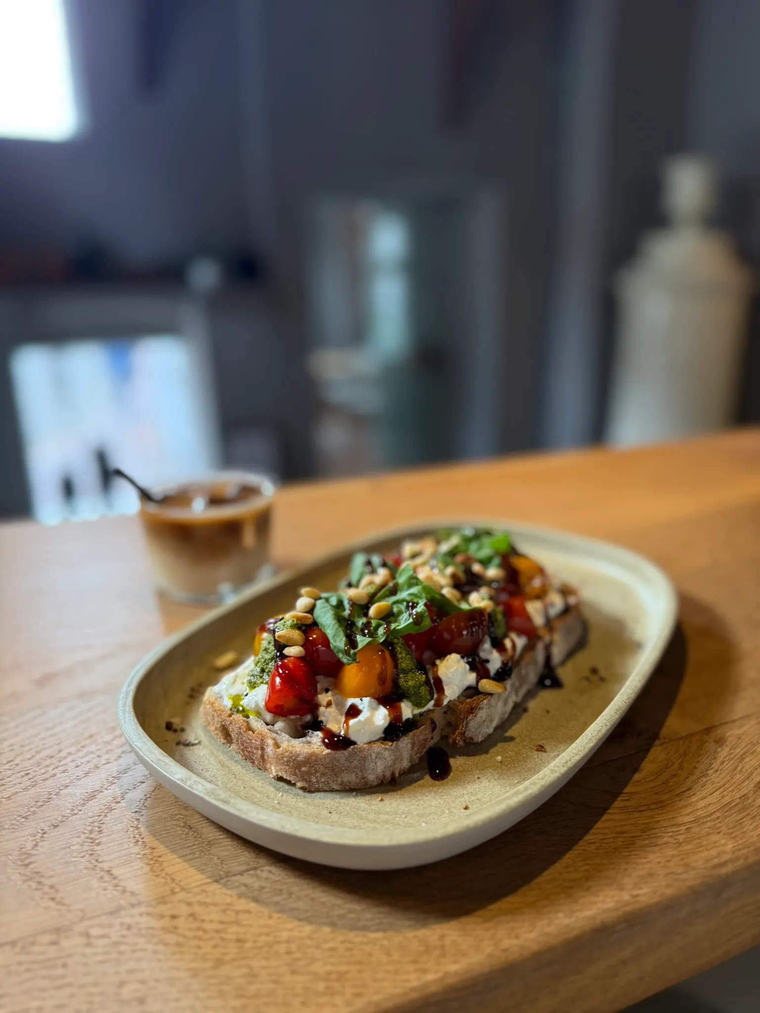 Tomaten-Burrata-Stulle mit Basilikum und Pinienkernen, dahinter ein Iced Latte